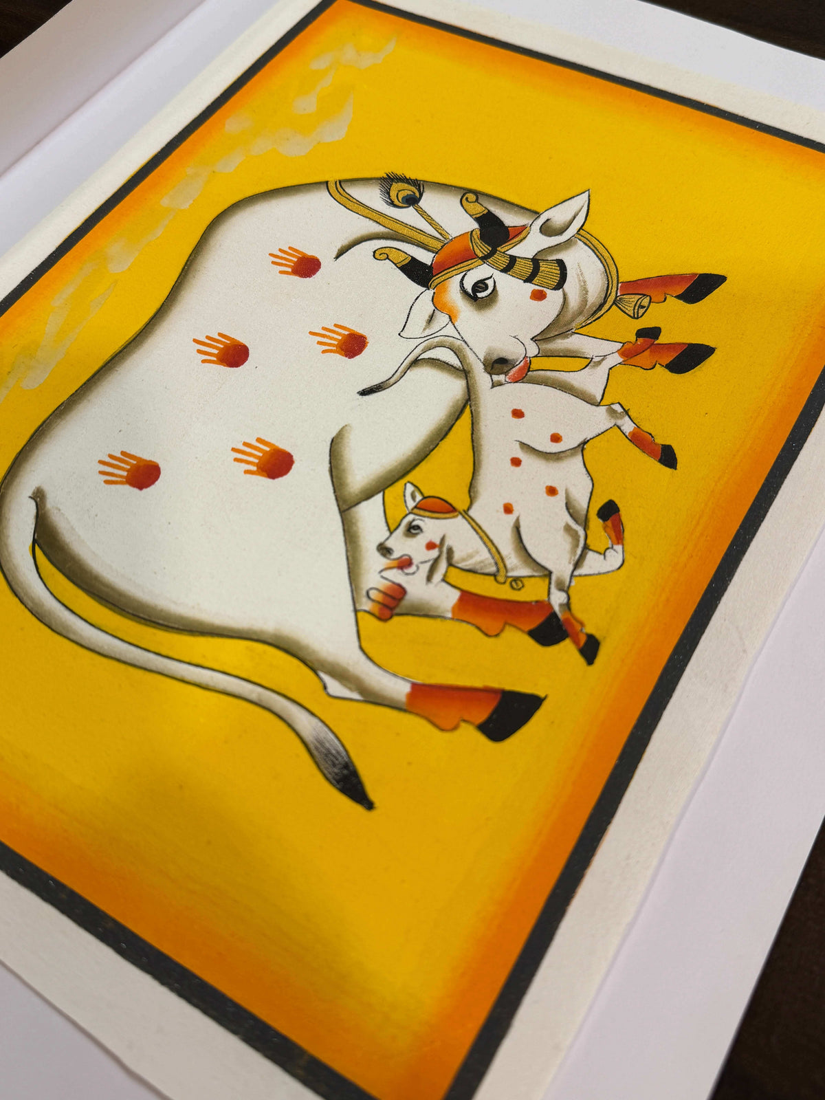 Original hand-painted Pichwai of cow and calf on yellow background with red handprints